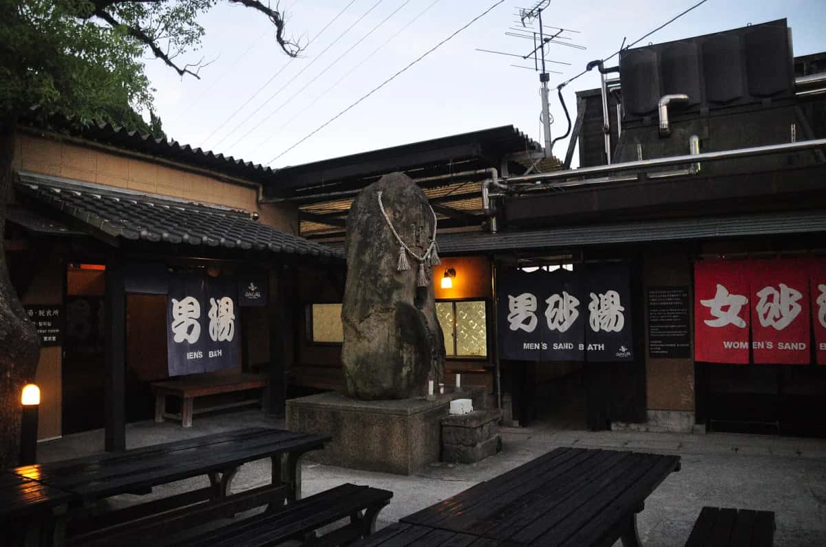 La cour de Hyotan Onsen à Beppu au crépuscule, avec les rideaux des bains de sable hommes et femmes et un grand rocher sacré