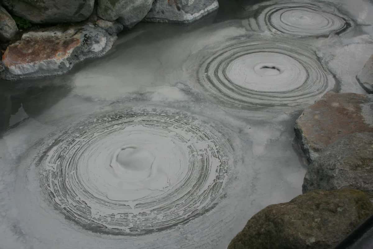 Bulles de boue grise éclatant en cercles concentriques dans un bassin entouré de roches à Beppu