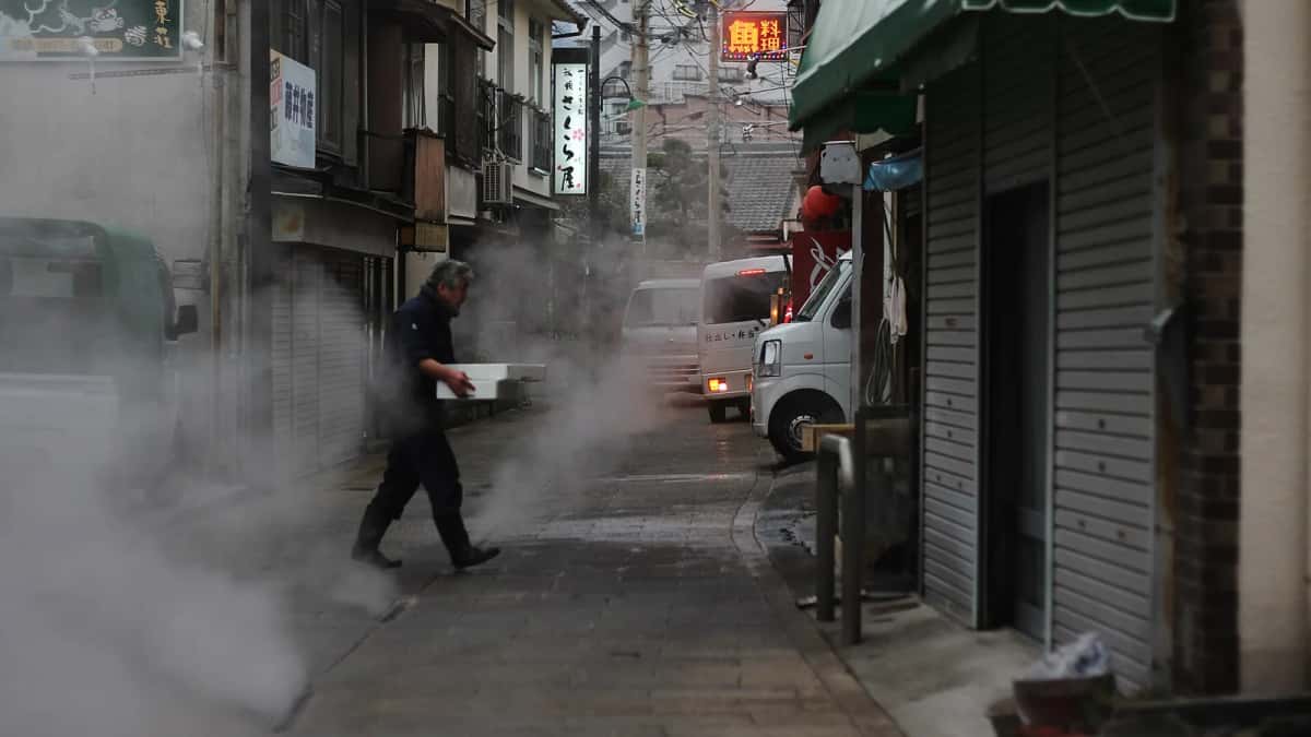 Un homme traverse une ruelle de Kannawa à Beppu envahie par la vapeur qui sort des bouches d'égout, entre des boutiques fermées