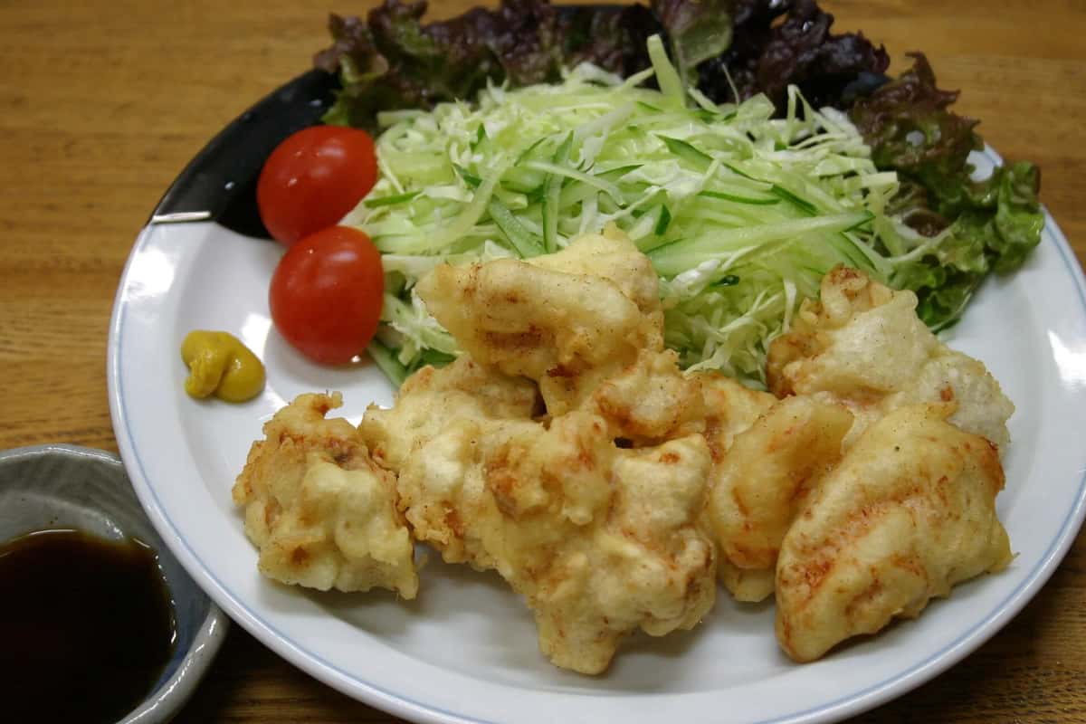 Une assiette de toriten, beignets de poulet d'Oita, avec du chou émincé, des tomates cerises, de la moutarde et une coupelle de sauce