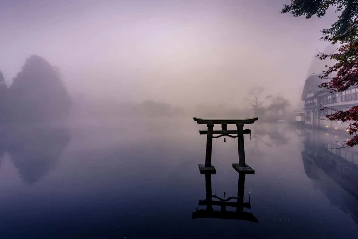 L'étang Kinrin de Yufuin dans la brume du matin, avec un torii de pierre dans l'eau et des feuilles d'érable rouges