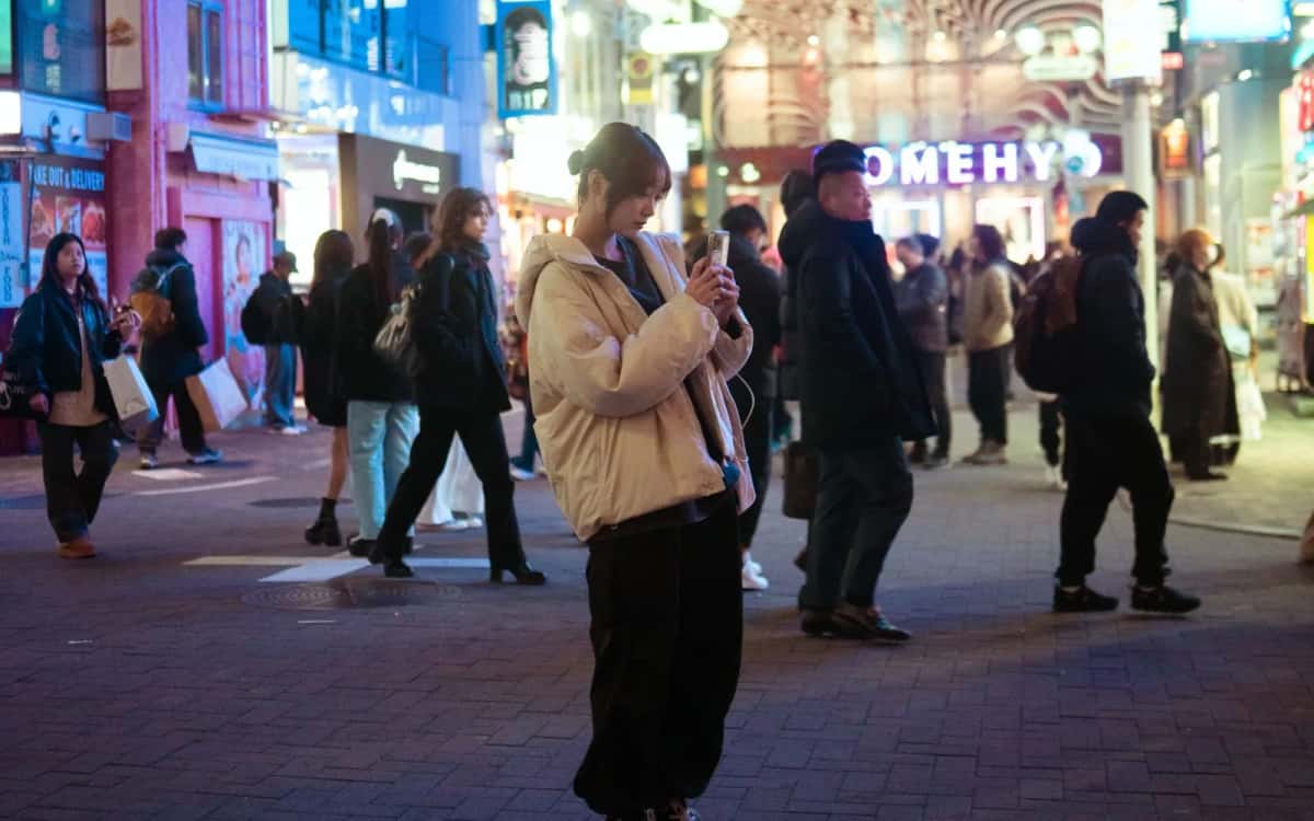 Voyageuse consultant son smartphone de nuit dans une rue animée de Shibuya, à Tokyo