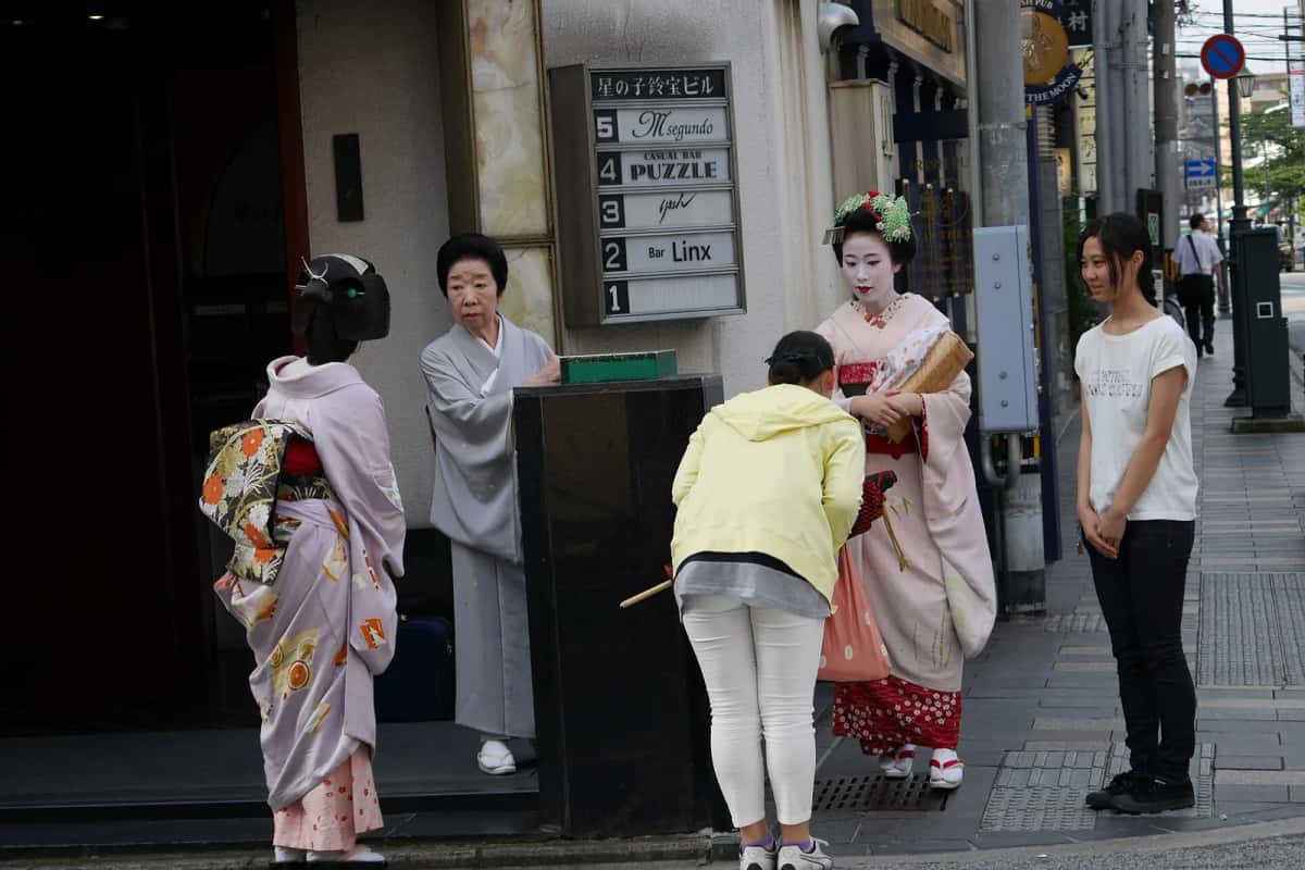 Une geiko en kimono sobre et une maiko à la coiffure fleurie dans une rue de Kyoto