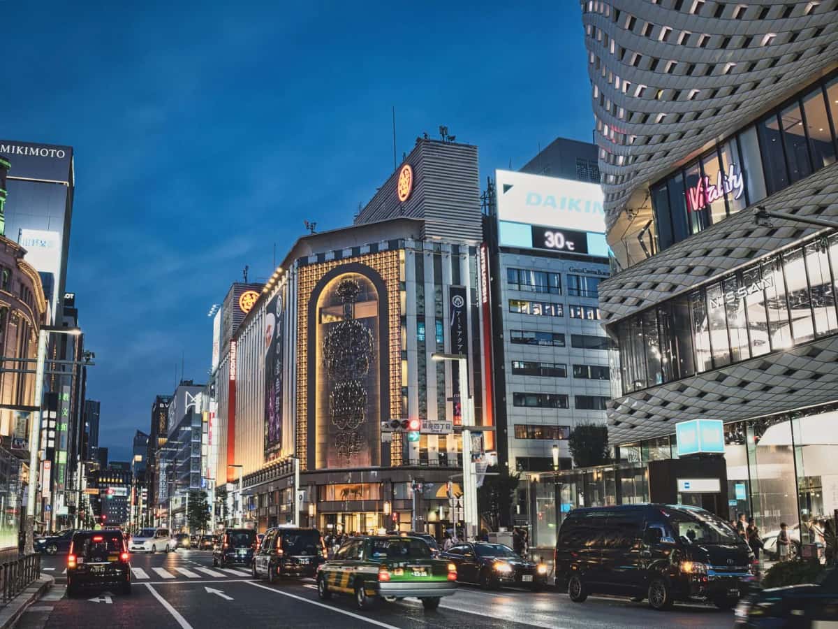 Le carrefour de Ginza 4-chome à la tombée de la nuit, avec les façades des grands magasins et les taxis