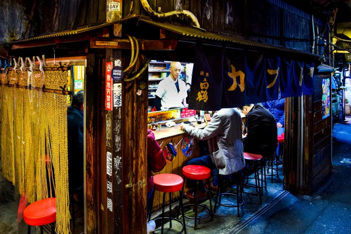 Comptoir d'izakaya avec tabourets rouges dans une ruelle de bars de Shinjuku le soir