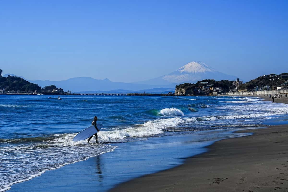Surfeur sur une plage de Kamakura, avec Enoshima et le mont Fuji au loin