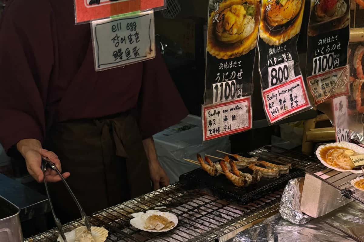 Marchand grillant des fruits de mer sur un étal du marché de rue d'Osaka, prix en yens
