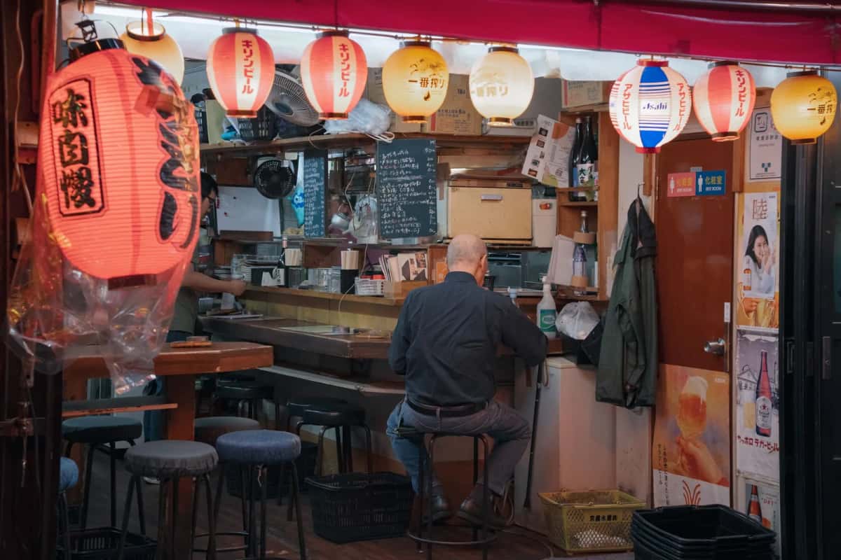 Comptoir d'un izakaya à Tokyo, lanternes en kanji et client attablé
