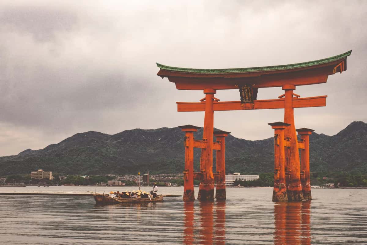 Une barque traditionnelle passe devant le grand torii vermillon d'Itsukushima, Miyajima