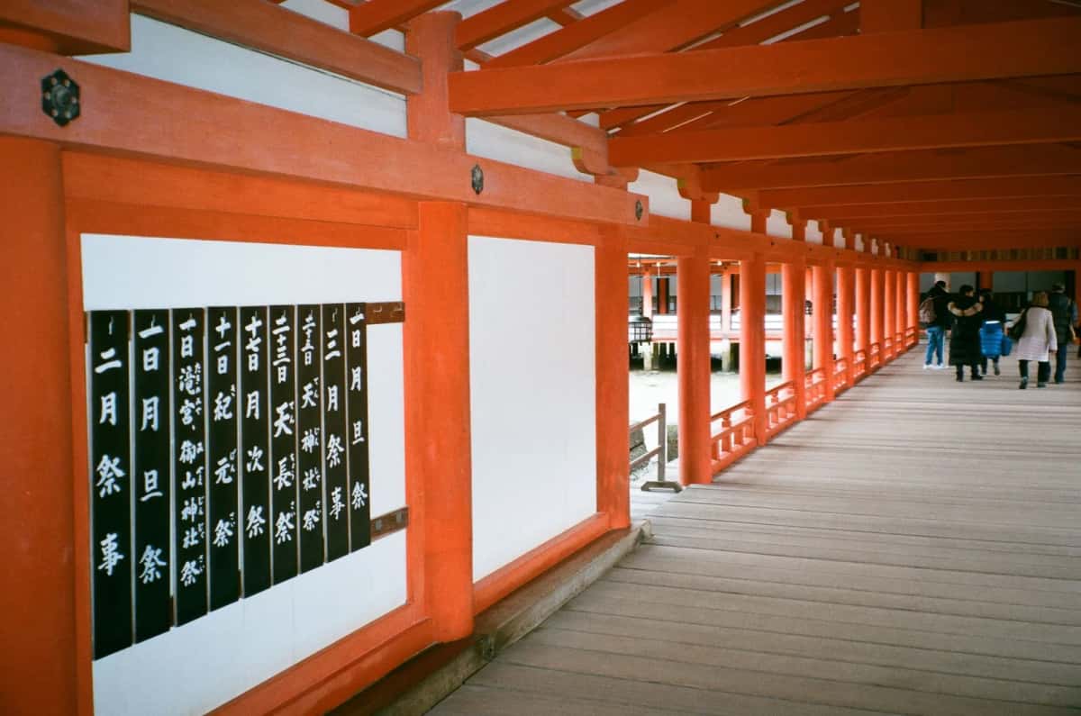 Galerie couverte vermillon du sanctuaire d'Itsukushima, avec les panneaux du calendrier des fêtes et des visiteurs