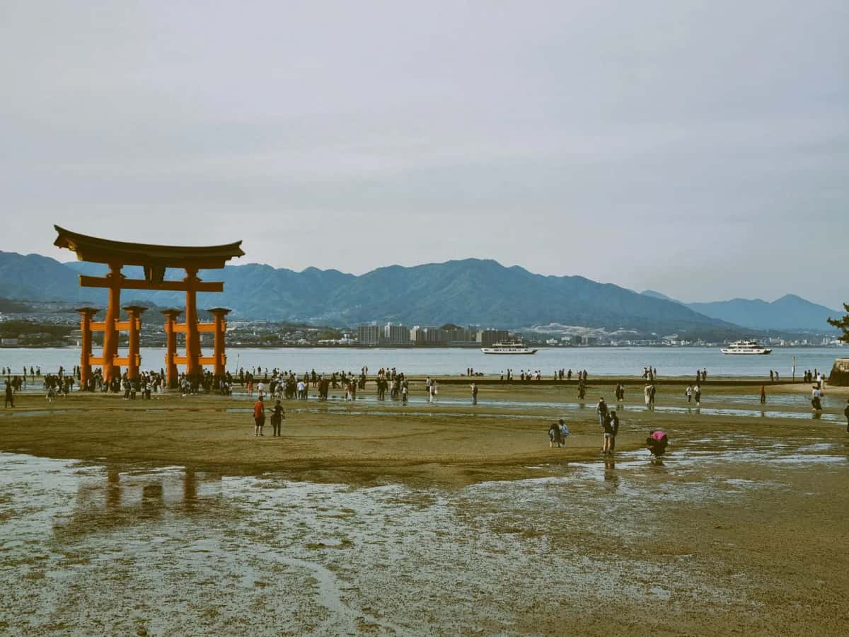 Des visiteurs marchent sur le sable humide autour du grand torii d'Itsukushima à marée basse, Miyajima