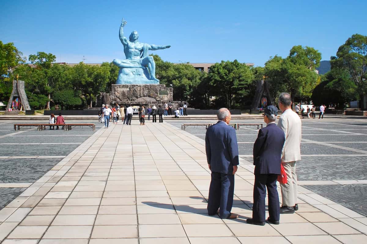 La statue de la Paix au fond de l'esplanade du parc de la Paix de Nagasaki, avec des visiteurs de dos