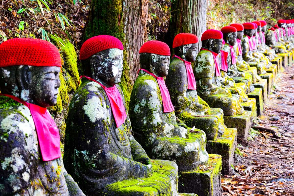 Rangée de statues jizō couvertes de mousse, coiffées de bonnets rouges, le long du sentier de Kanmangafuchi à Nikko