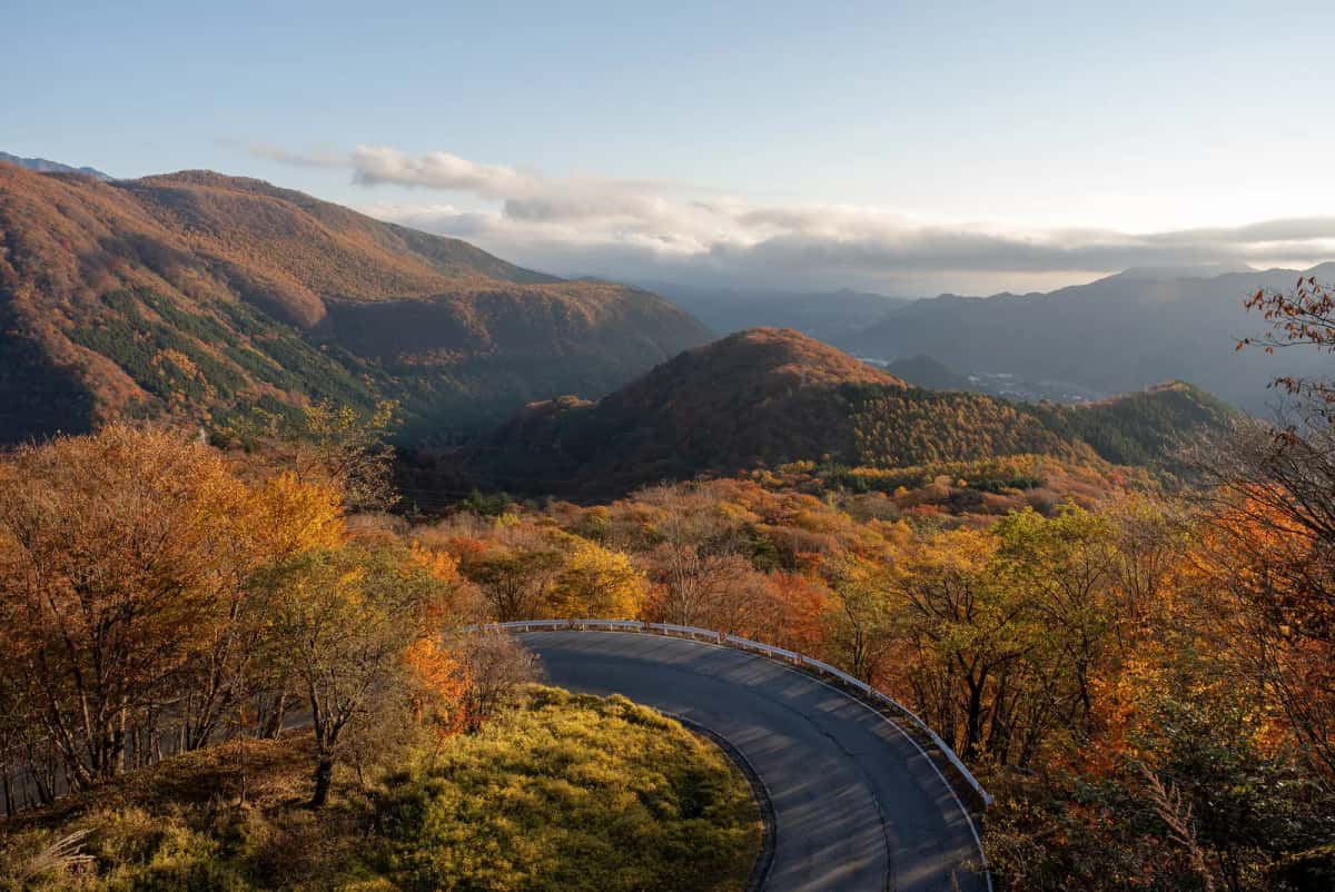 Un virage de la route d'Irohazaka entre des montagnes couvertes de feuillages orange et roux, à Nikko