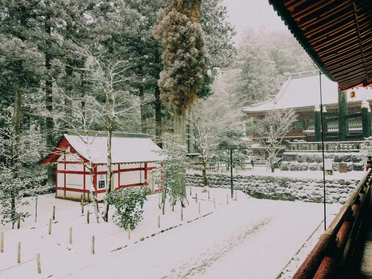 Les bâtiments rouges et blancs du Tōshō-gū de Nikko sous la neige, entourés d'arbres enneigés
