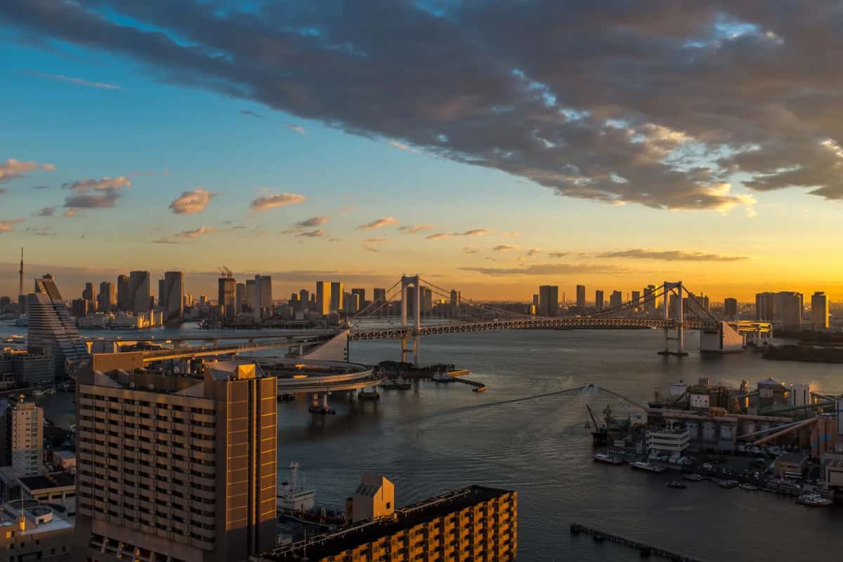 La baie de Tokyo au coucher du soleil vue d'en haut, avec le Rainbow Bridge et les tours de la ville sous un ciel orange et bleu