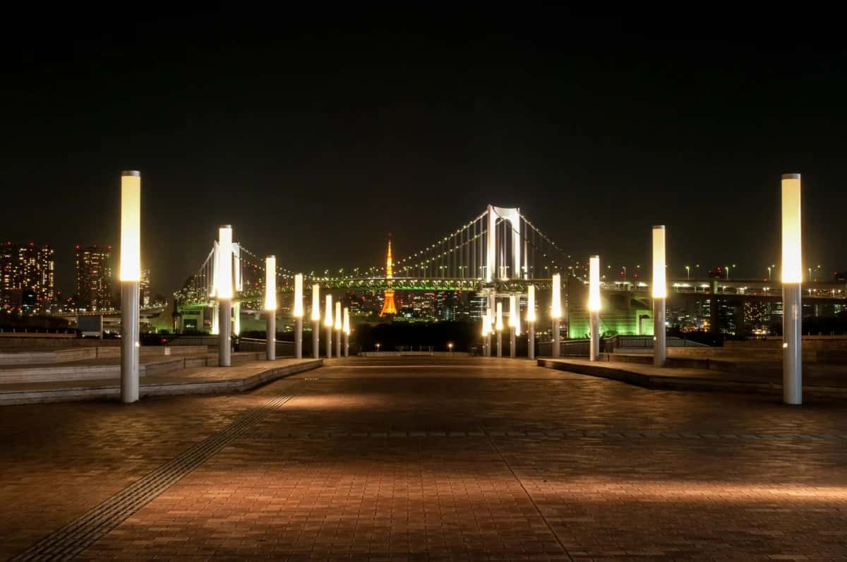 Le front de mer d'Odaiba la nuit, avec ses lampadaires face au Rainbow Bridge et à la Tokyo Tower illuminée