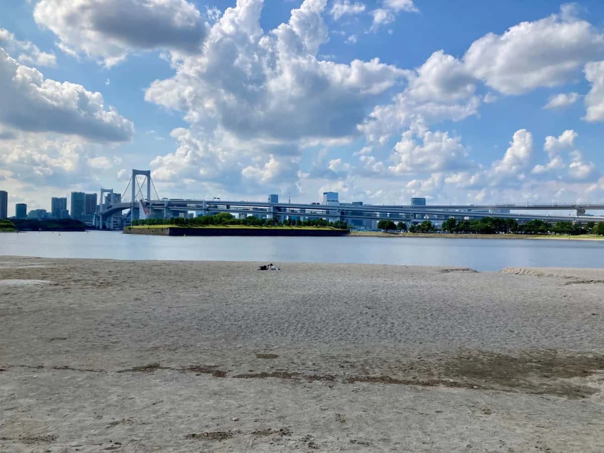 La plage de sable d'Odaiba Kaihin Koen sous un ciel bleu, avec le Rainbow Bridge au fond