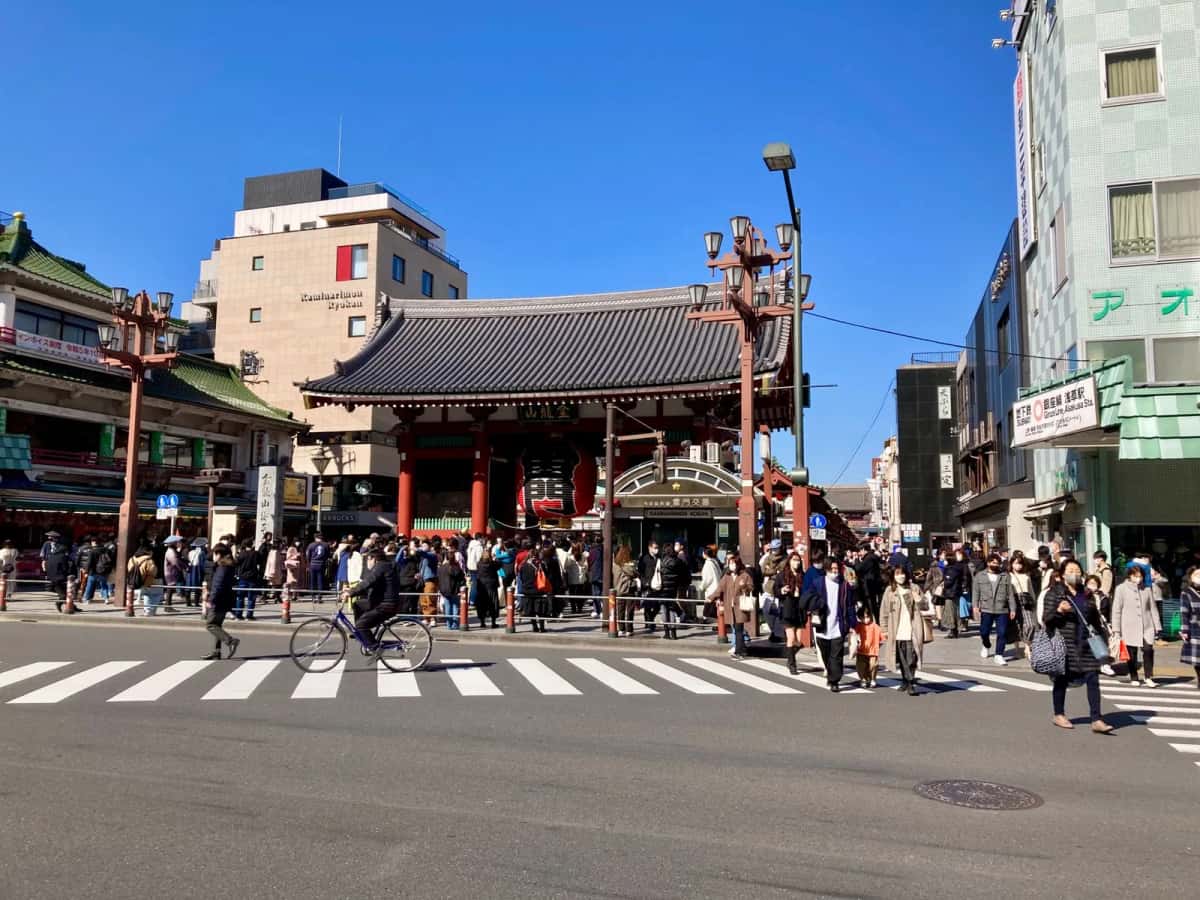 Passants traversant une rue ensoleillée devant la porte Kaminarimon du Senso-ji à Asakusa, Tokyo