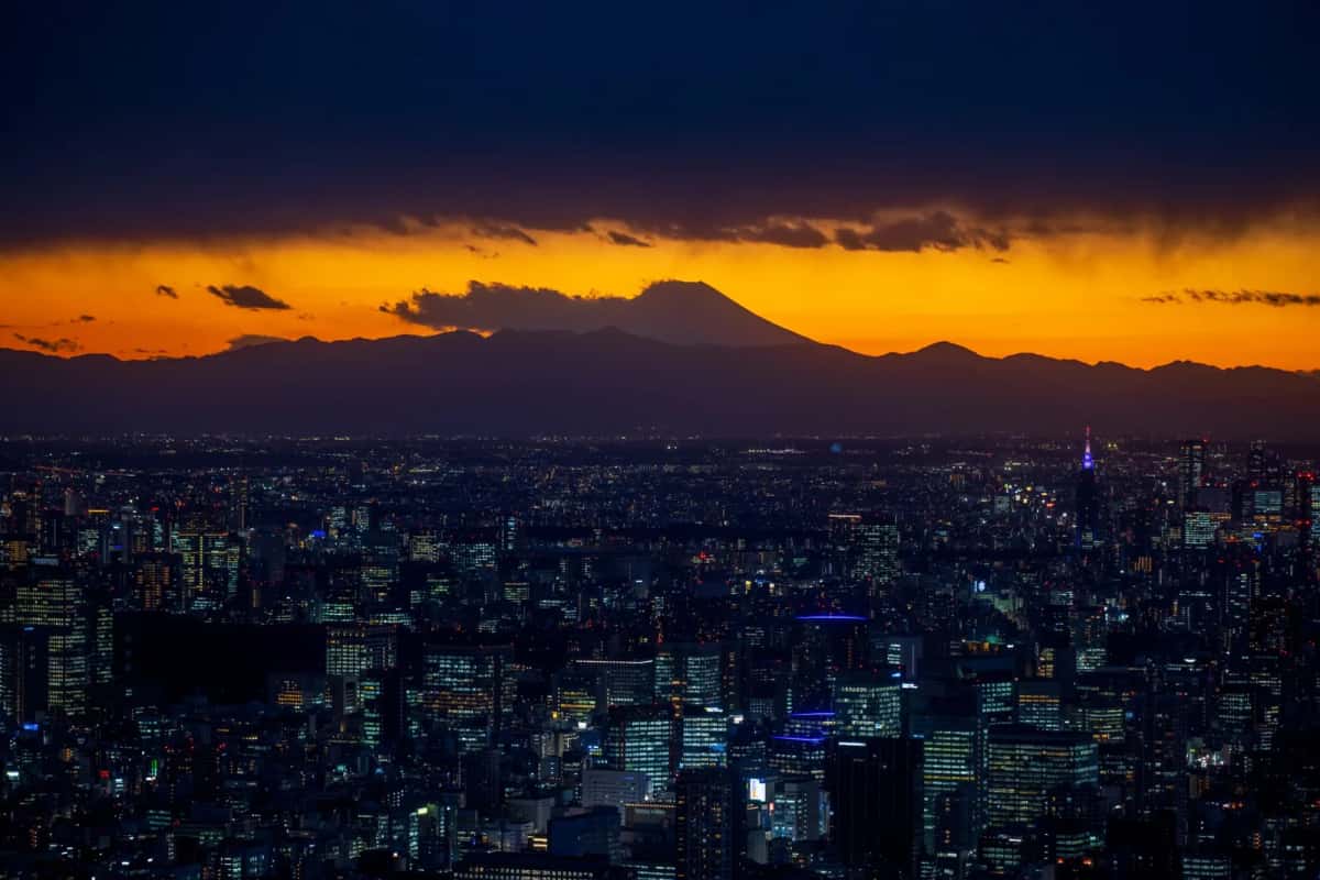 Silhouette du mont Fuji sous un ciel orange au coucher du soleil, au-dessus des immeubles de Tokyo