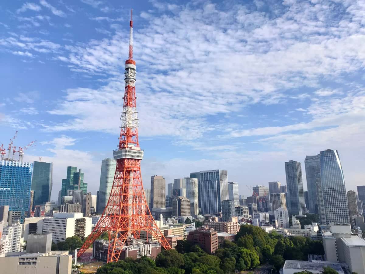 La Tokyo Tower rouge et blanche sous un ciel bleu nuageux, entourée des gratte-ciel de Minato à Tokyo