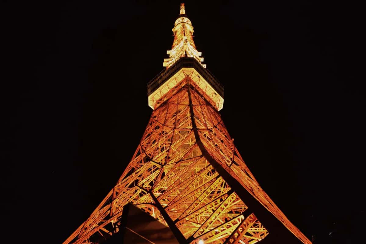 La Tokyo Tower illuminée en orange la nuit, vue en contre-plongée depuis son pied