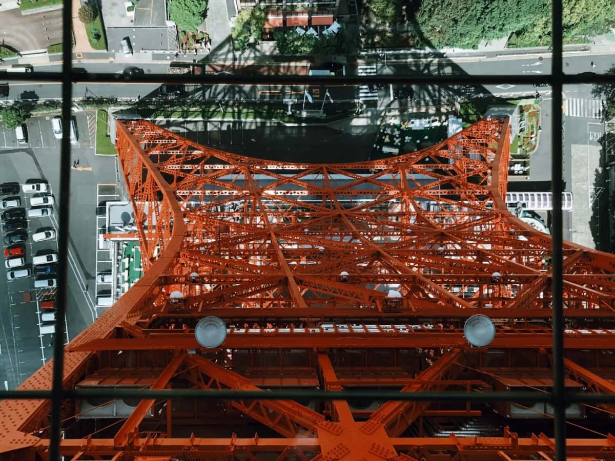 Vue plongeante à travers une vitre du Main Deck sur la structure métallique rouge de la Tokyo Tower et le sol en bas