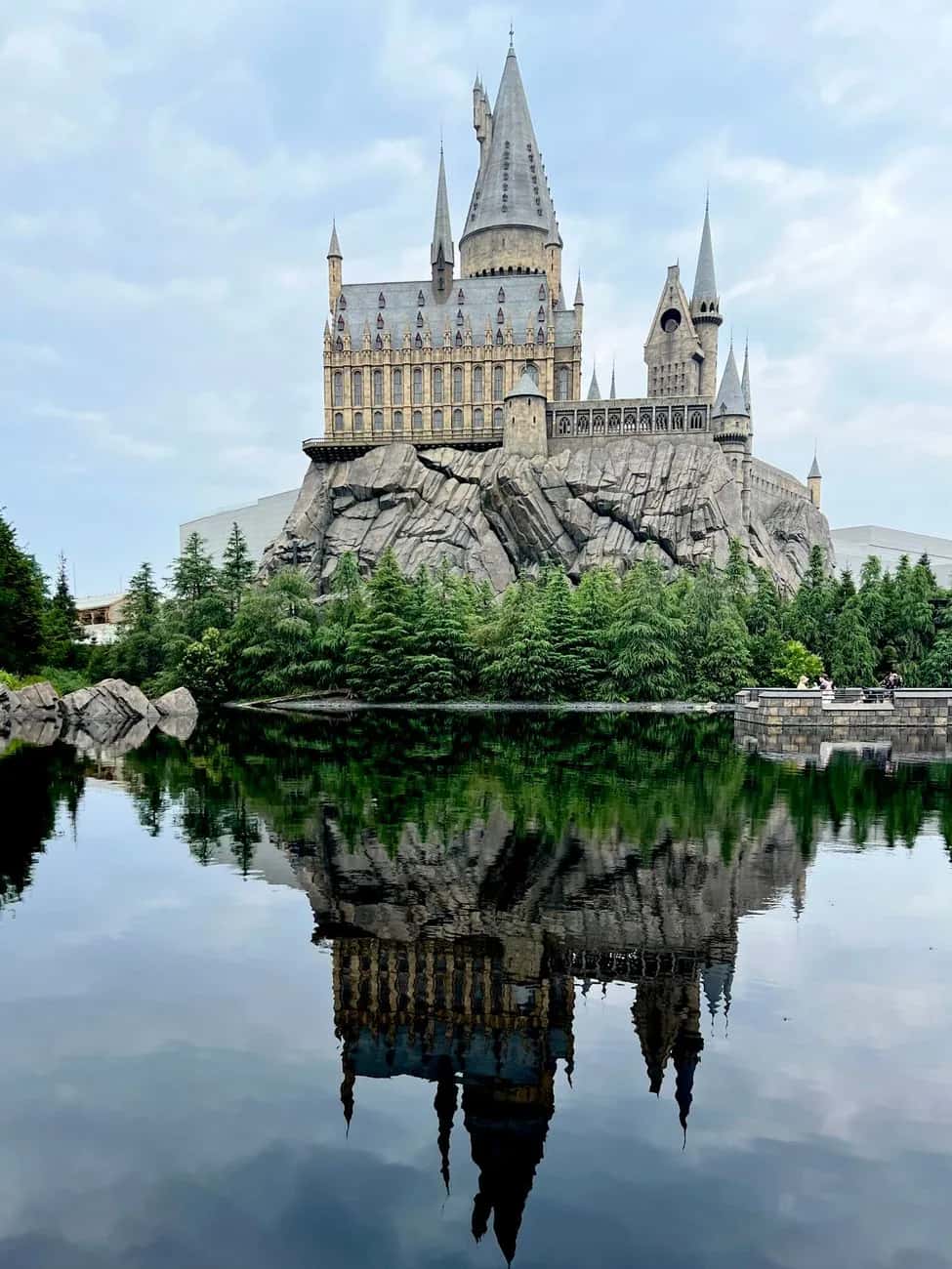 Le château de Poudlard de Universal Studios Japan à Osaka qui se reflète dans le lac, entouré de sapins